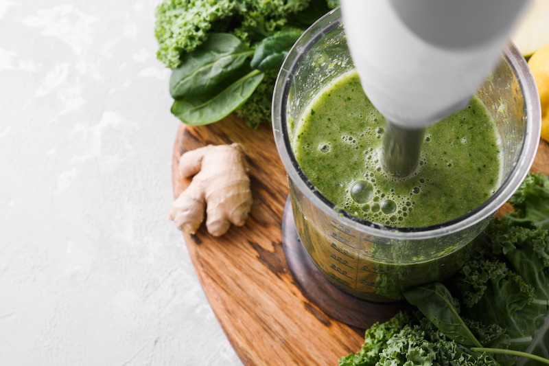 Cooking green smoothie in a blender on a light background. Close up. Fresh green smoothie in a blender. Top view. Freshly prepared vegetarian smoothies from shpenata cabbage and kale.