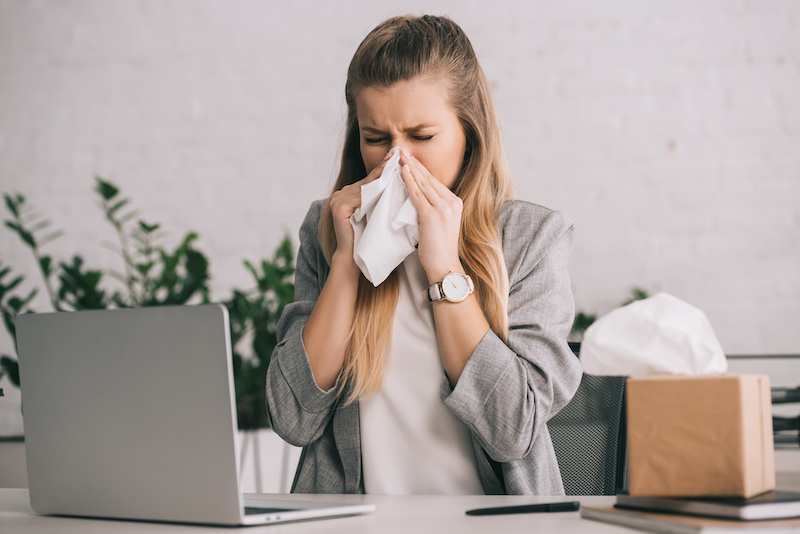 woman sneezing at her office desk